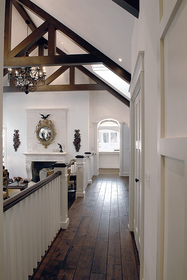 Inspiration pour un grand salon traditionnel avec un mur blanc, parquet foncé, une cheminée standard, un manteau de cheminée en pierre, un sol marron et poutres apparentes.