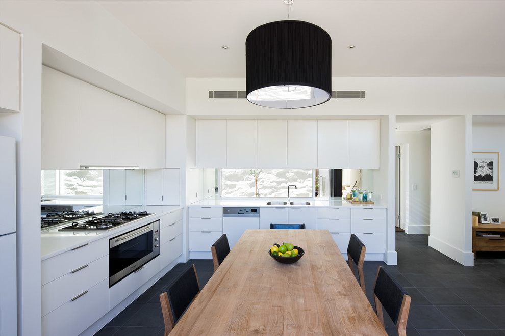 Mid-sized contemporary l-shaped eat-in kitchen in Adelaide with white cabinets, a double-bowl sink, flat-panel cabinets, mirror splashback, white appliances and no island.