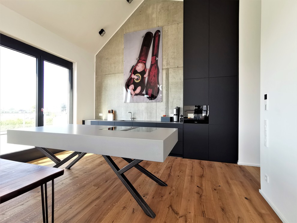 This is an example of a large contemporary open plan kitchen in Munich with an undermount sink, flat-panel cabinets, black cabinets, stainless steel benchtops, black appliances, with island, brown floor and grey benchtop.