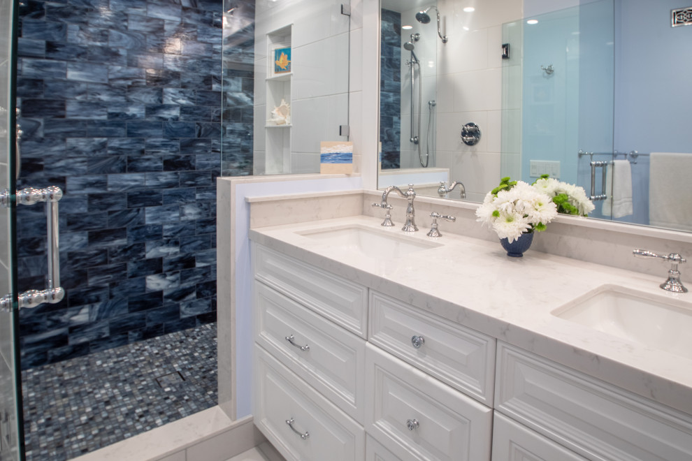 Идея дизайна: главная ванная комната среднего размера в морском стиле с фасадами с выступающей филенкой, белыми фасадами, душем в нише, унитазом-моноблоком, синей плиткой, стеклянной плиткой, белыми стенами, полом из керамогранита, врезной раковиной, столешницей из искусственного кварца, белым полом, душем с распашными дверями, белой столешницей, нишей, тумбой под две раковины и встроенной тумбой