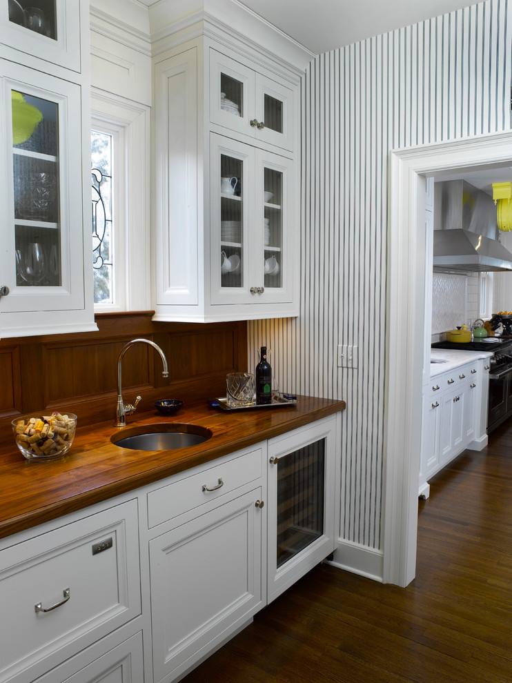 Example of a transitional medium tone wood floor kitchen pantry design in New York with white cabinets, ceramic backsplash, stainless steel appliances, an island, an undermount sink and wood countertops