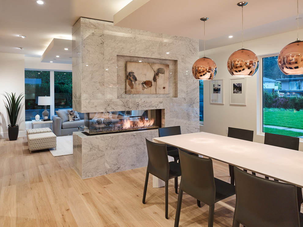 This is an example of a large modern open plan dining in Vancouver with white walls, light hardwood floors, a two-sided fireplace, a tile fireplace surround and beige floor.