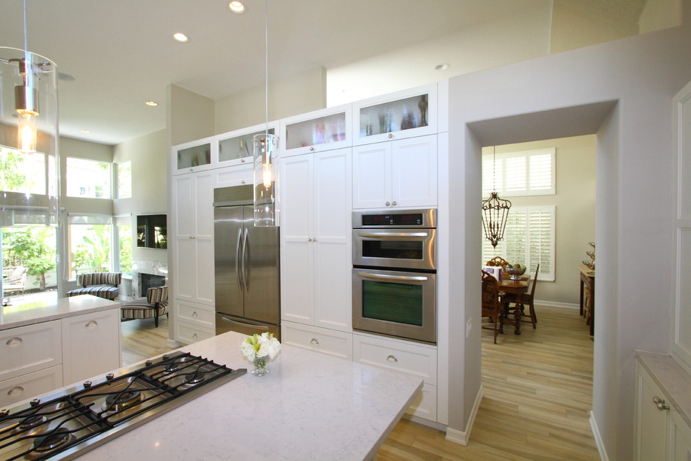 Photo of a large beach style separate kitchen in Los Angeles with an undermount sink, recessed-panel cabinets, white cabinets, granite benchtops, grey splashback, glass tile splashback, stainless steel appliances, porcelain floors and a peninsula.