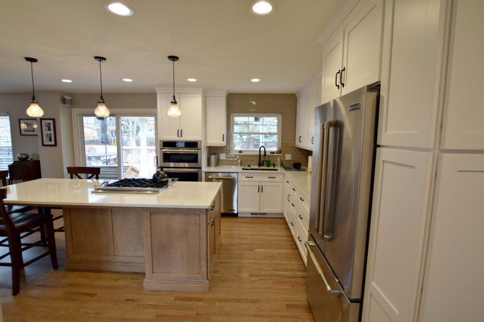 Inspiration for a large transitional u-shaped open plan kitchen in Denver with an undermount sink, shaker cabinets, white cabinets, quartz benchtops, subway tile splashback, stainless steel appliances, medium hardwood floors, with island and white benchtop.