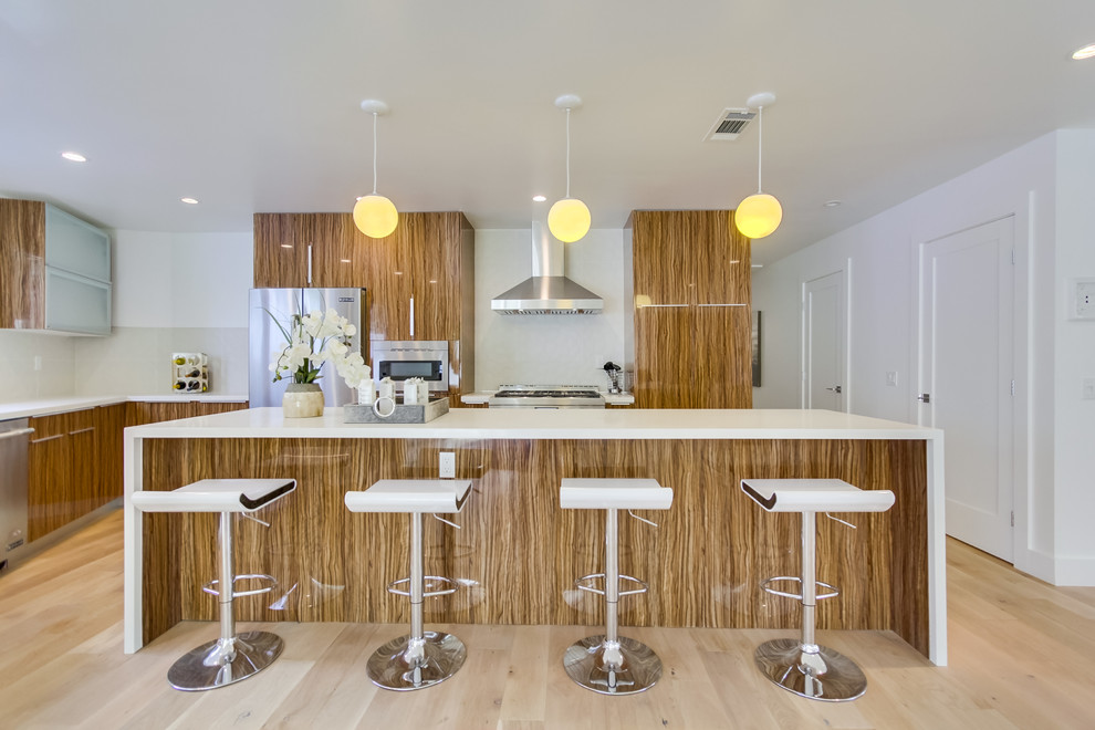 Photo of a large contemporary l-shaped eat-in kitchen in San Diego with flat-panel cabinets, brown cabinets, quartz benchtops, white splashback, porcelain splashback, stainless steel appliances, laminate floors and with island.