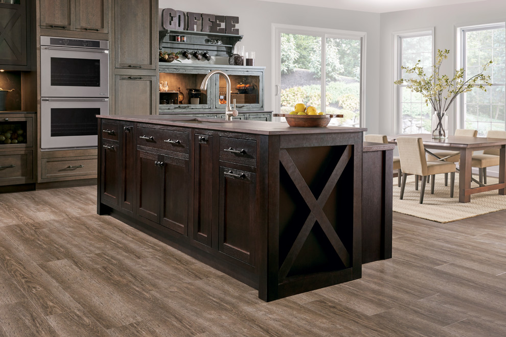 This is an example of a country eat-in kitchen in Other with an undermount sink, beaded inset cabinets, dark wood cabinets, stainless steel appliances, medium hardwood floors, with island and brown floor.
