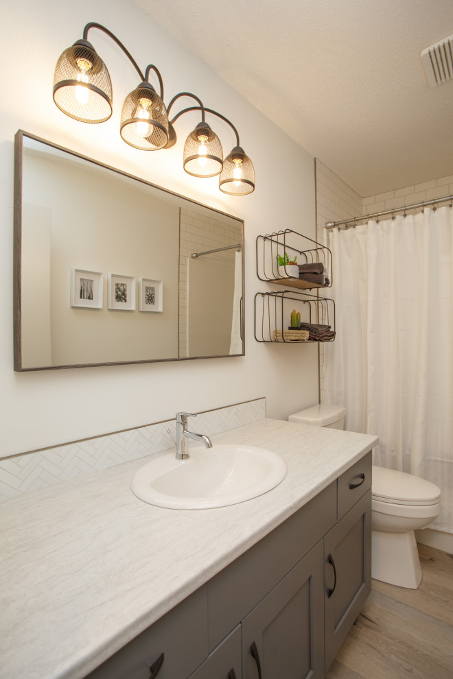 Photo of a small beach style kids bathroom in Calgary with shaker cabinets, grey cabinets, an alcove tub, an alcove shower, a one-piece toilet, white tile, ceramic tile, white walls, vinyl floors, a drop-in sink, laminate benchtops, beige floor, a shower curtain, white benchtops, a single vanity and a built-in vanity.
