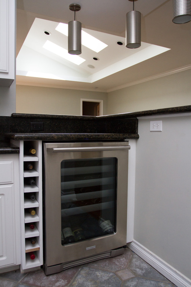 This is an example of a small contemporary l-shaped seated home bar in Los Angeles with raised-panel cabinets, white cabinets, granite benchtops, black splashback and multi-coloured floor.