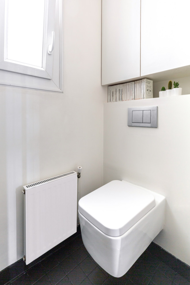 Photo of a small contemporary powder room in Paris with beaded inset cabinets, white cabinets, a wall-mount toilet, gray tile, ceramic tile, white walls, ceramic floors, a wall-mount sink and grey floor.