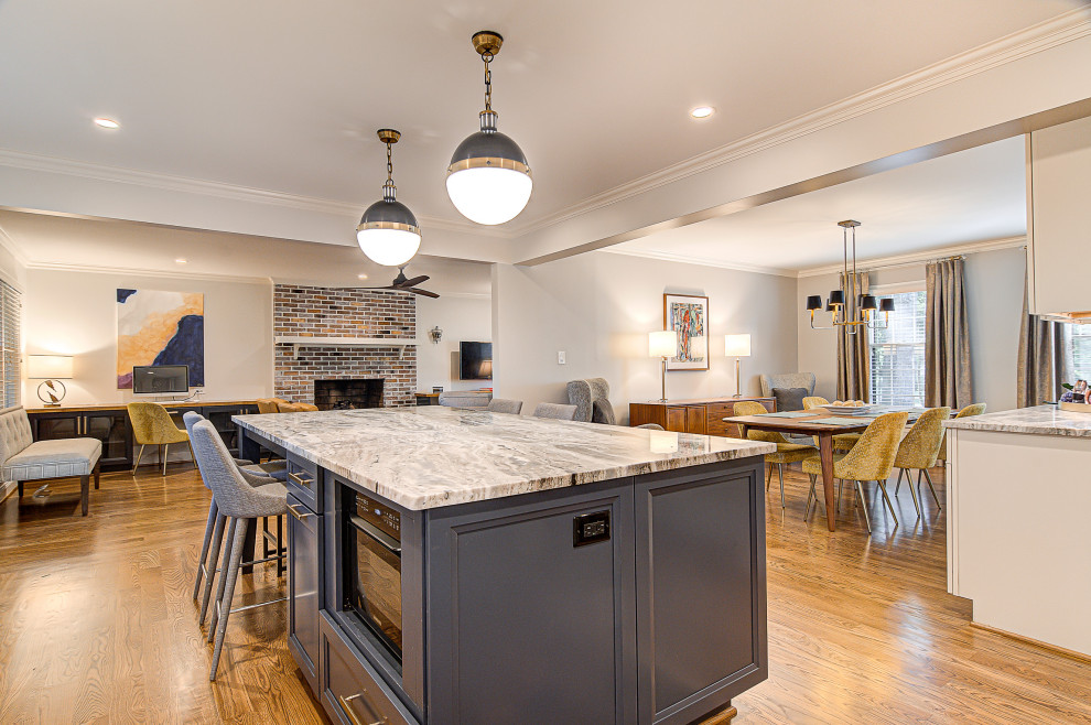Mid-sized transitional l-shaped medium tone wood floor and brown floor eat-in kitchen photo with a farmhouse sink, recessed-panel cabinets, white cabinets, marble countertops, white backsplash, subway tile backsplash, stainless steel appliances, an island and gray countertops