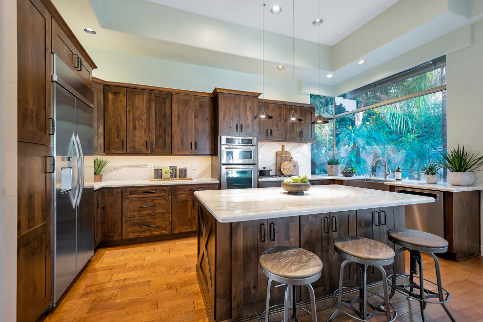 Example of a large transitional u-shaped open concept kitchen design in Phoenix with a farmhouse sink, shaker cabinets, dark wood cabinets, quartz countertops, white backsplash, quartz backsplash, stainless steel appliances, an island and white countertops