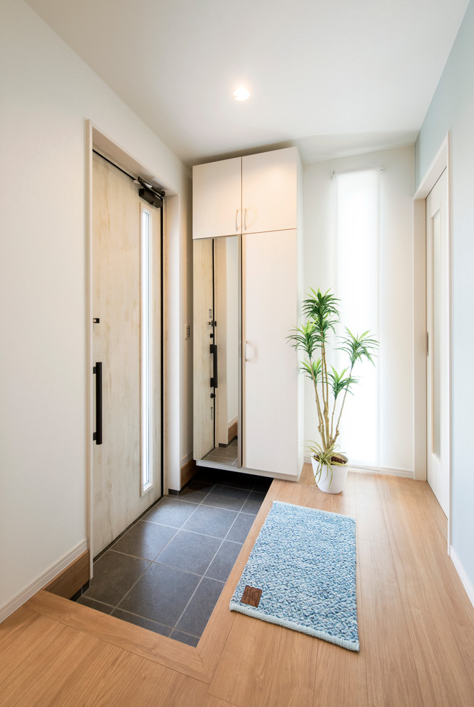 Small beach style entryway in Fukuoka with white walls, a single front door, a light wood front door and black floor.