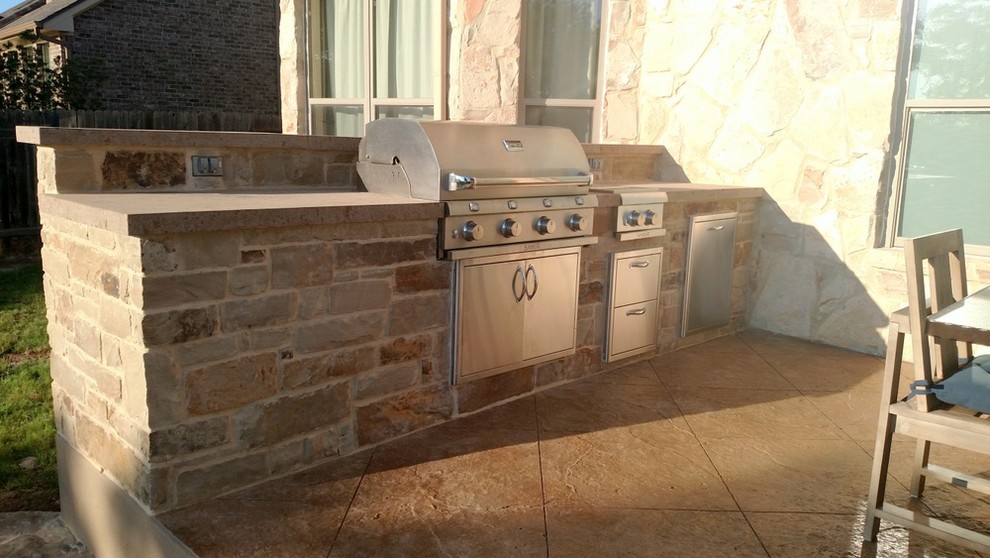 Large country backyard patio in Austin with an outdoor kitchen, natural stone pavers and a roof extension.