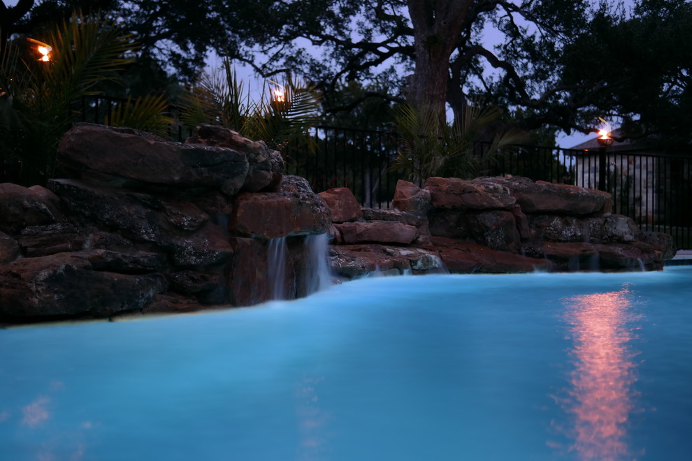Inspiration for a mid-sized backyard custom-shaped natural pool in Austin with a water feature and stamped concrete.