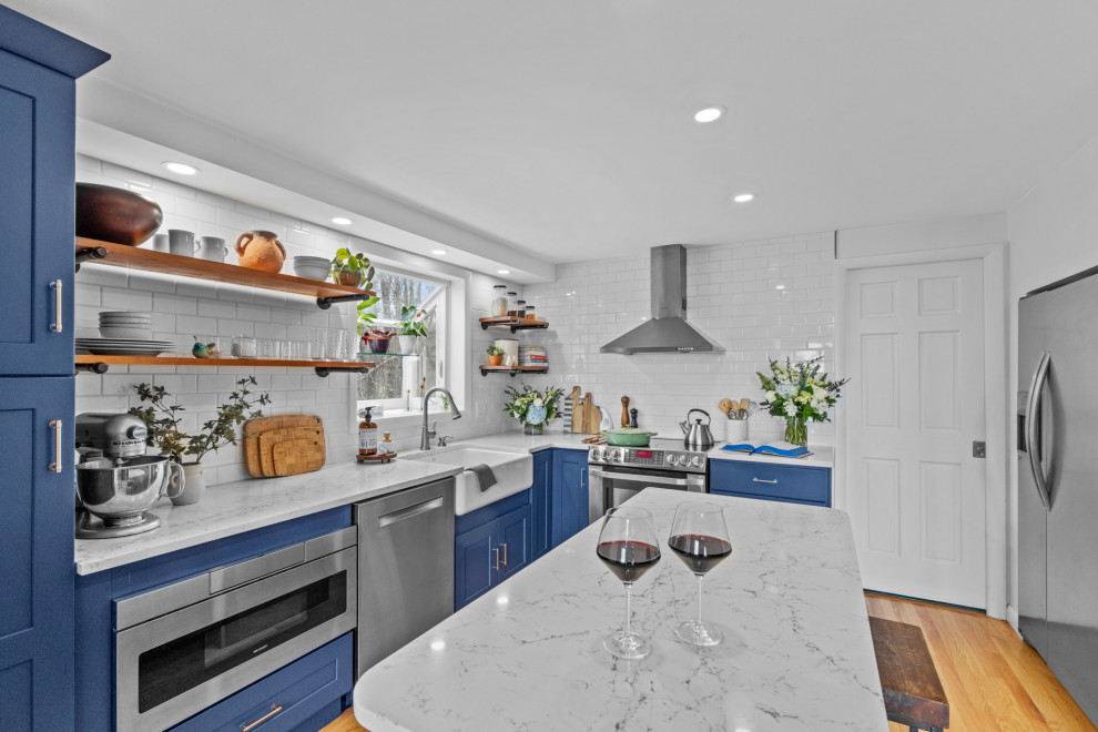 Inspiration for a traditional l-shaped kitchen in Providence with a belfast sink, shaker cabinets, blue cabinets, white splashback, ceramic splashback, stainless steel appliances, medium hardwood flooring, an island and white worktops.