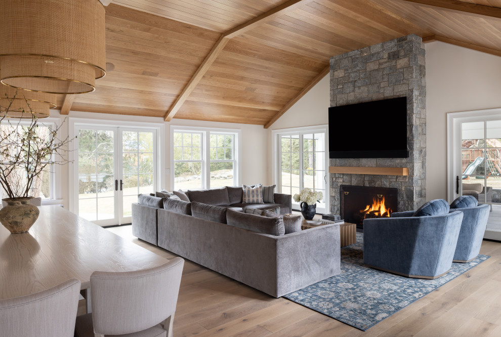 Example of a large transitional open concept light wood floor and shiplap ceiling living room design in New York with a two-sided fireplace, a stone fireplace and a wall-mounted tv