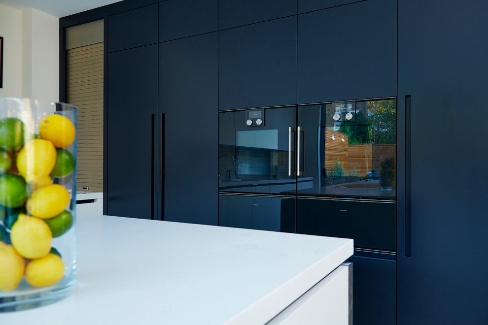 Large contemporary l-shaped eat-in kitchen in London with an integrated sink, flat-panel cabinets, white cabinets, solid surface benchtops, metallic splashback, panelled appliances, ceramic floors and with island.