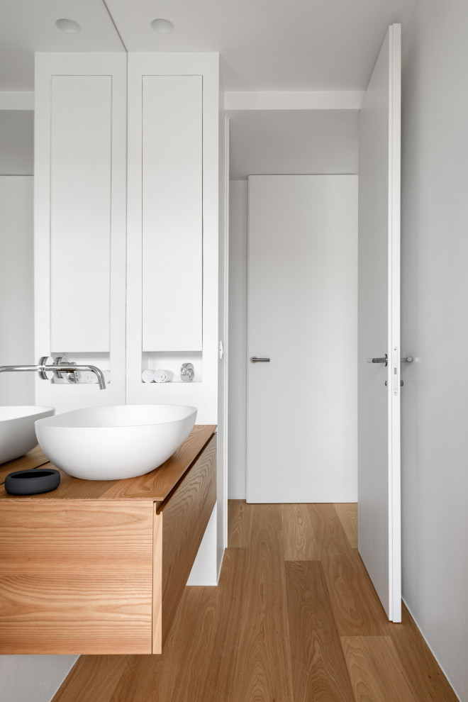 This is an example of a mid-sized contemporary 3/4 wet room bathroom in Venice with beaded inset cabinets, light wood cabinets, a two-piece toilet, white tile, mirror tile, white walls, light hardwood floors, a vessel sink, solid surface benchtops, beige floor, a hinged shower door, white benchtops, a niche, a single vanity and a floating vanity.