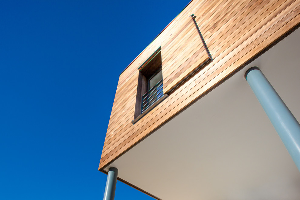 Cette photo montre une façade de maison beige tendance en bois de taille moyenne et à un étage avec un toit plat.