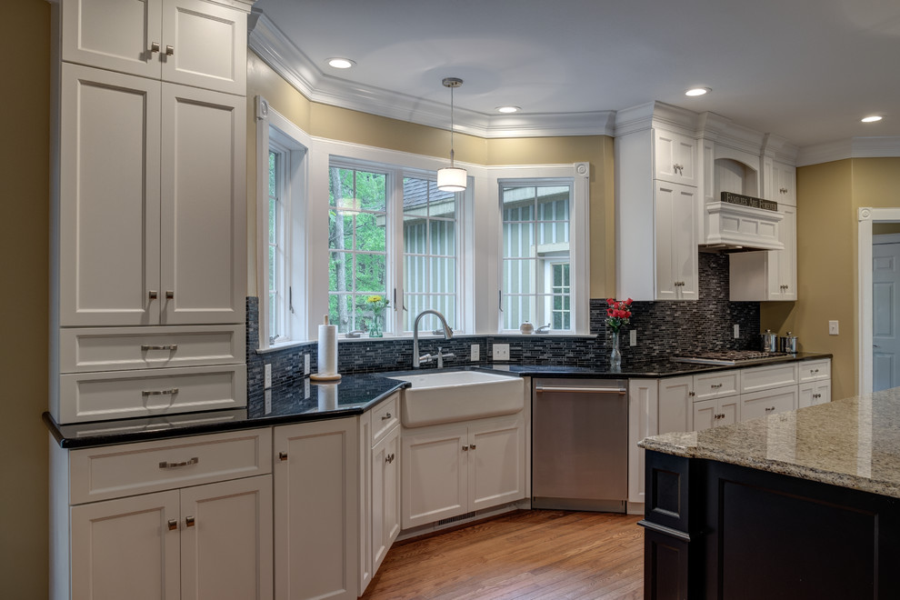 This is an example of a mid-sized country kitchen in Other with a farmhouse sink, recessed-panel cabinets, white cabinets, black splashback, stainless steel appliances, medium hardwood floors and with island.