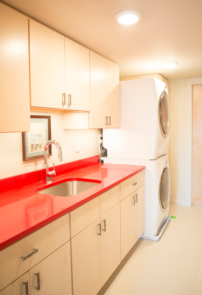Photo of a contemporary single-wall dedicated laundry room in St Louis with flat-panel cabinets, white walls, a stacked washer and dryer, red benchtop and an undermount sink.