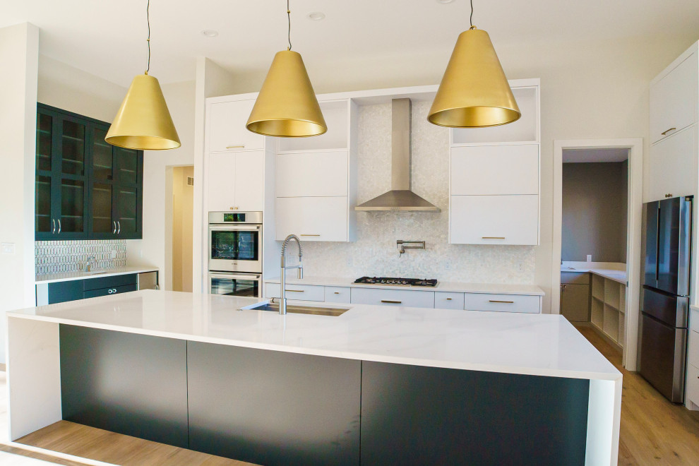 This is an example of a large contemporary u-shaped open plan kitchen in St Louis with a submerged sink, flat-panel cabinets, white cabinets, quartz worktops, white splashback, mosaic tiled splashback, stainless steel appliances, vinyl flooring, an island, brown floors and white worktops.