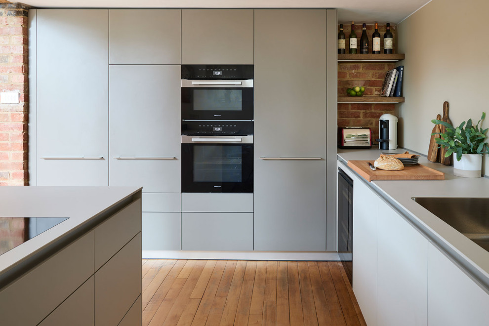 Mid-sized minimalist u-shaped medium tone wood floor and exposed beam open concept kitchen photo in Oxfordshire with an integrated sink, flat-panel cabinets, white cabinets, laminate countertops, glass sheet backsplash, black appliances, a peninsula and white countertops