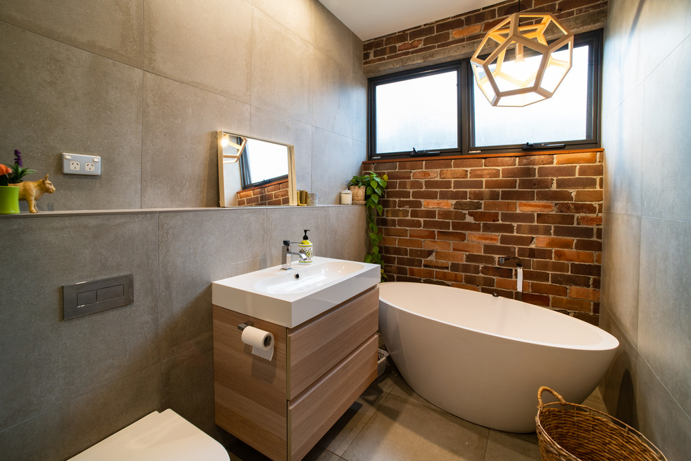 Photo of a mid-sized contemporary bathroom in Sydney with light wood cabinets, a freestanding tub, an open shower, a one-piece toilet, gray tile, porcelain tile, multi-coloured walls, porcelain floors, a vessel sink, engineered quartz benchtops, grey floor, an open shower and grey benchtops.