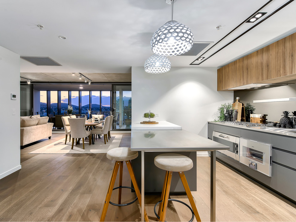 Design ideas for a contemporary galley kitchen in Brisbane with flat-panel cabinets, grey cabinets, stainless steel benchtops, grey splashback, light hardwood floors, a peninsula, beige floor and grey benchtop.