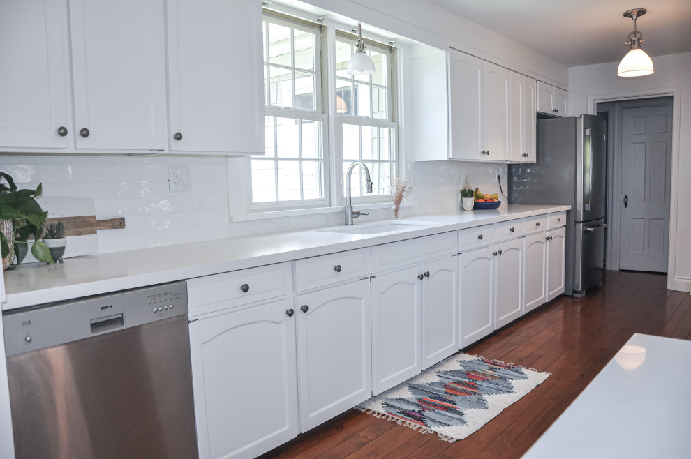 Inspiration for a large transitional galley dark wood floor and brown floor kitchen pantry remodel in Toronto with an undermount sink, raised-panel cabinets, white cabinets, quartz countertops, white backsplash, ceramic backsplash, stainless steel appliances, two islands and white countertops