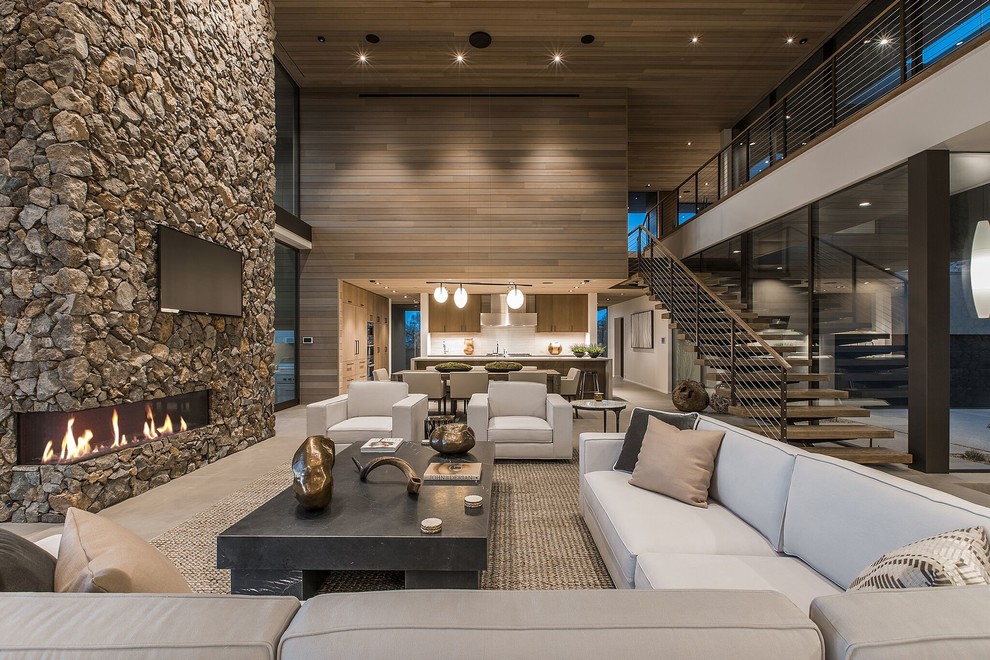 This is an example of an expansive contemporary open concept living room in Las Vegas with brown walls, a corner fireplace, a stone fireplace surround, a wall-mounted tv and beige floor.