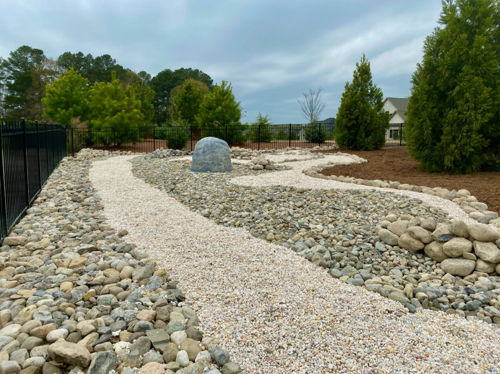 Inspiration for an expansive traditional backyard full sun xeriscape for summer in Charlotte with with flowerbed, river rock and a metal fence.