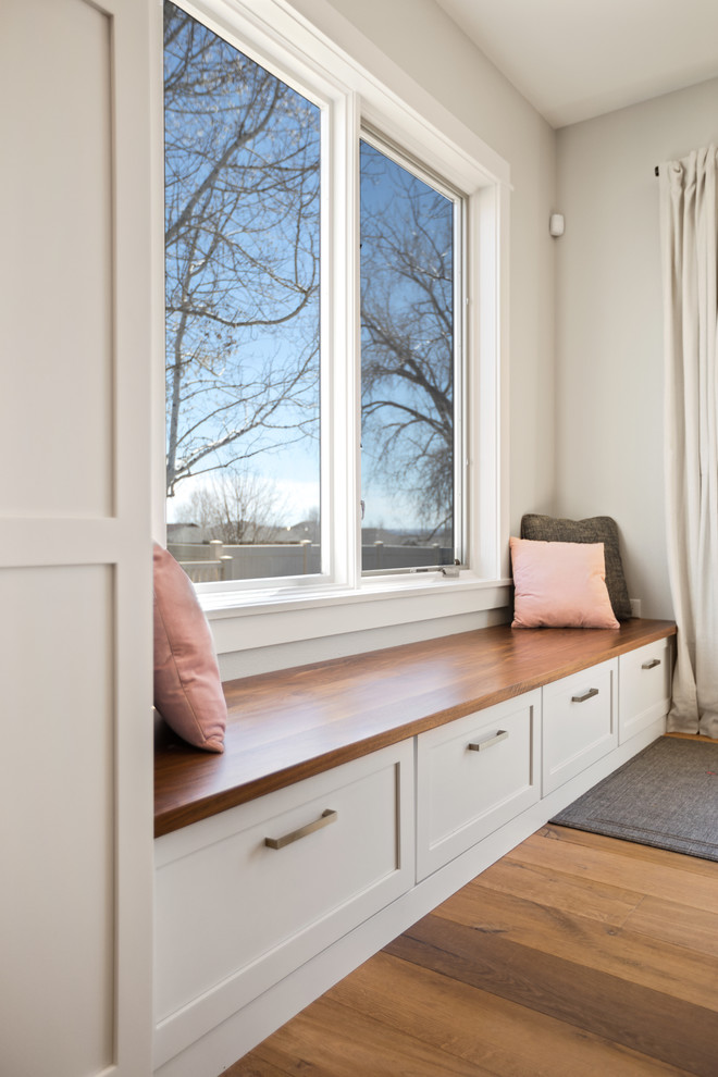 Example of a transitional l-shaped light wood floor and brown floor kitchen design with a farmhouse sink, shaker cabinets, white cabinets, quartz countertops, white backsplash, subway tile backsplash, stainless steel appliances, an island and white countertops