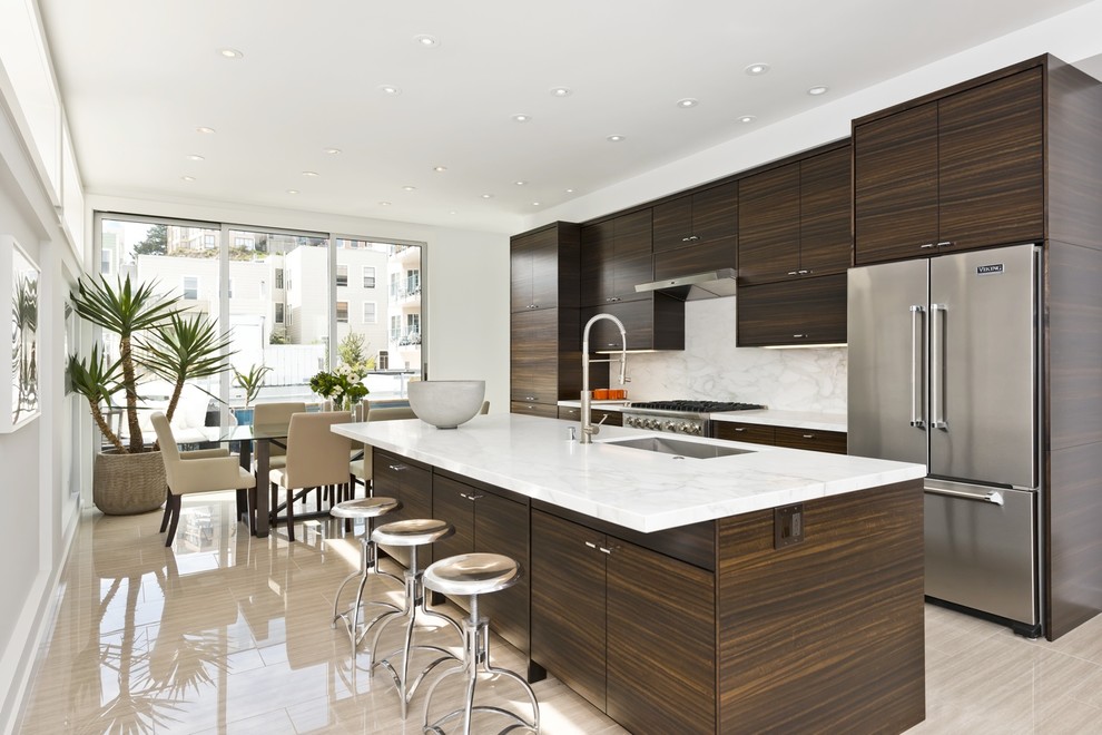 Design ideas for a contemporary galley open plan kitchen in San Francisco with an undermount sink, flat-panel cabinets, dark wood cabinets, white splashback, stainless steel appliances, with island and beige floor.