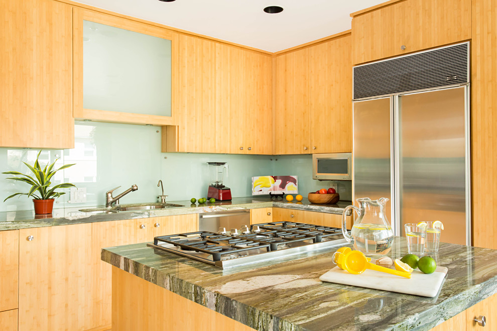 Photo of a mid-sized beach style u-shaped eat-in kitchen in Los Angeles with a double-bowl sink, flat-panel cabinets, light wood cabinets, granite benchtops, blue splashback, glass sheet splashback, stainless steel appliances, porcelain floors, with island and grey floor.