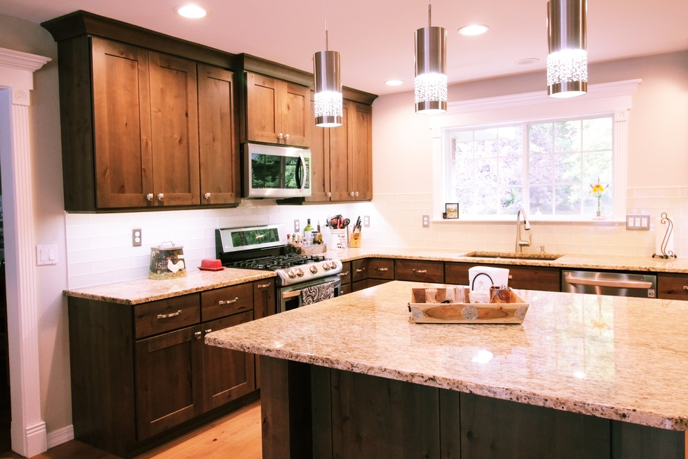 Inspiration for a large rustic u-shaped light wood floor and brown floor open concept kitchen remodel in Boise with an undermount sink, shaker cabinets, brown cabinets, granite countertops, white backsplash, glass tile backsplash, stainless steel appliances and an island