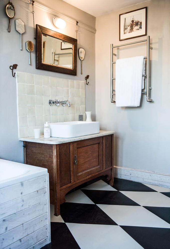 This is an example of a small traditional bathroom in London with recessed-panel cabinets, medium wood cabinets, a drop-in tub, black and white tile, white walls and a trough sink.
