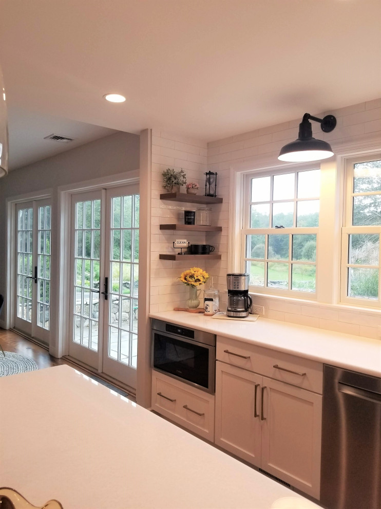 Large country l-shaped eat-in kitchen in New York with a farmhouse sink, shaker cabinets, white cabinets, marble benchtops, yellow splashback, ceramic splashback, stainless steel appliances, medium hardwood floors, with island, brown floor, white benchtop and exposed beam.