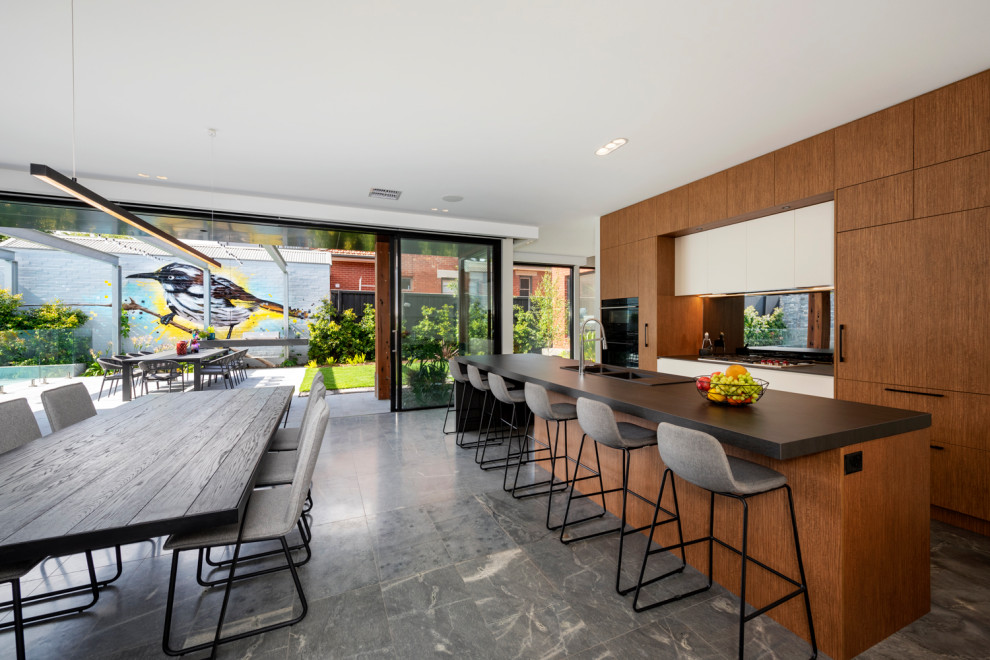 This is an example of a large contemporary galley open plan kitchen in Melbourne with a double-bowl sink, flat-panel cabinets, mirror splashback, black appliances, limestone floors and with island.