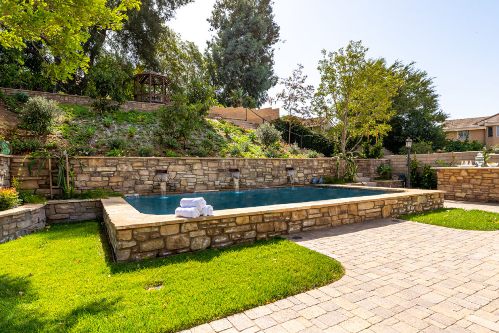 Photo of an expansive mediterranean backyard rectangular aboveground pool in Los Angeles with natural stone pavers.