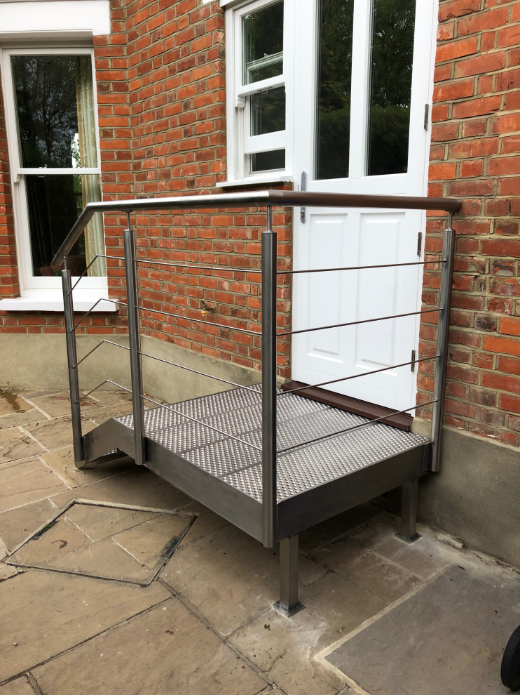 This is an example of a small contemporary metal straight staircase in London with open risers, metal railing and brick walls.