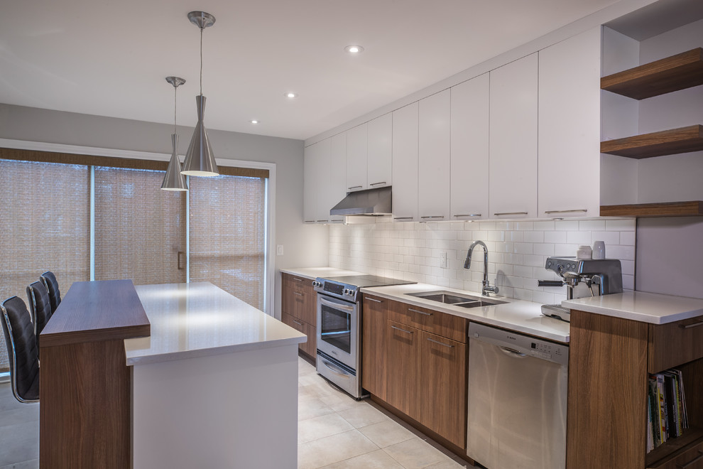 Design ideas for a mid-sized modern single-wall kitchen in Montreal with an undermount sink, flat-panel cabinets, white cabinets, quartz benchtops, white splashback, subway tile splashback, stainless steel appliances, ceramic floors, with island, white floor and white benchtop.