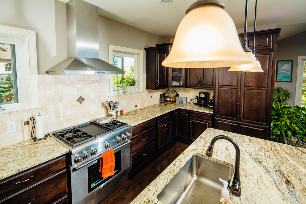 Photo of an arts and crafts l-shaped eat-in kitchen in Philadelphia with an undermount sink, raised-panel cabinets, dark wood cabinets, granite benchtops, brown splashback, cement tile splashback, stainless steel appliances, medium hardwood floors and with island.
