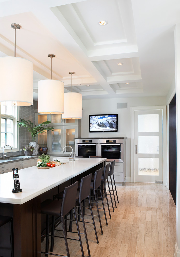 Large transitional u-shaped light wood floor and brown floor enclosed kitchen photo in Chicago with an undermount sink, shaker cabinets, white cabinets, quartz countertops, gray backsplash, mosaic tile backsplash, stainless steel appliances and an island