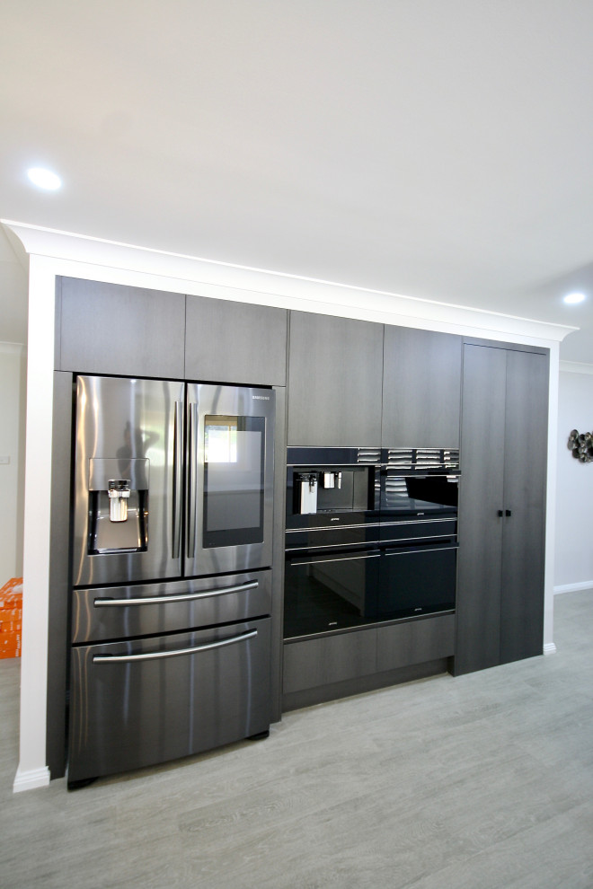 This is an example of a large modern u-shaped open plan kitchen in Sydney with an undermount sink, flat-panel cabinets, white cabinets, quartz benchtops, grey splashback, stone slab splashback, white appliances, medium hardwood floors, multiple islands, brown floor and grey benchtop.