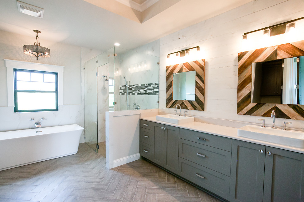 Large country master bathroom in Dallas with shaker cabinets, blue cabinets, a freestanding tub, a curbless shower, gray tile, marble, white walls, ceramic floors, a drop-in sink, granite benchtops, grey floor and a hinged shower door.