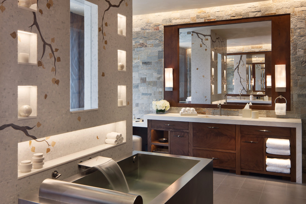 This is an example of an expansive contemporary master bathroom in Denver with flat-panel cabinets, dark wood cabinets, a freestanding tub, an open shower, a wall-mount toilet, multi-coloured tile, stone slab, multi-coloured walls, porcelain floors, an integrated sink, limestone benchtops, grey floor and a hinged shower door.