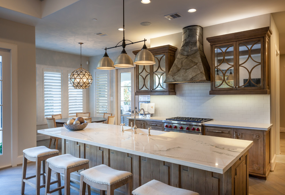 Huge transitional single-wall medium tone wood floor and brown floor open concept kitchen photo in Houston with a farmhouse sink, glass-front cabinets, medium tone wood cabinets, white backsplash, subway tile backsplash, an island, stainless steel appliances and white countertops