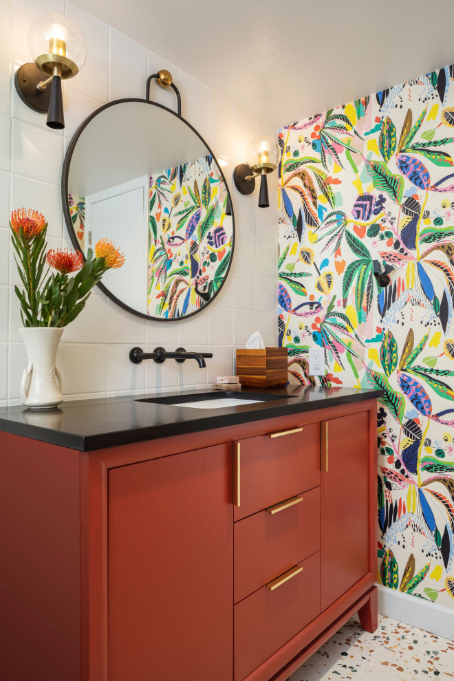 This is an example of a mid-sized eclectic kids bathroom in Denver with flat-panel cabinets, red cabinets, an alcove tub, a shower/bathtub combo, a one-piece toilet, white tile, porcelain tile, multi-coloured walls, terrazzo floors, an undermount sink, engineered quartz benchtops, multi-coloured floor, a shower curtain, black benchtops, a niche, a single vanity, a freestanding vanity and wallpaper.
