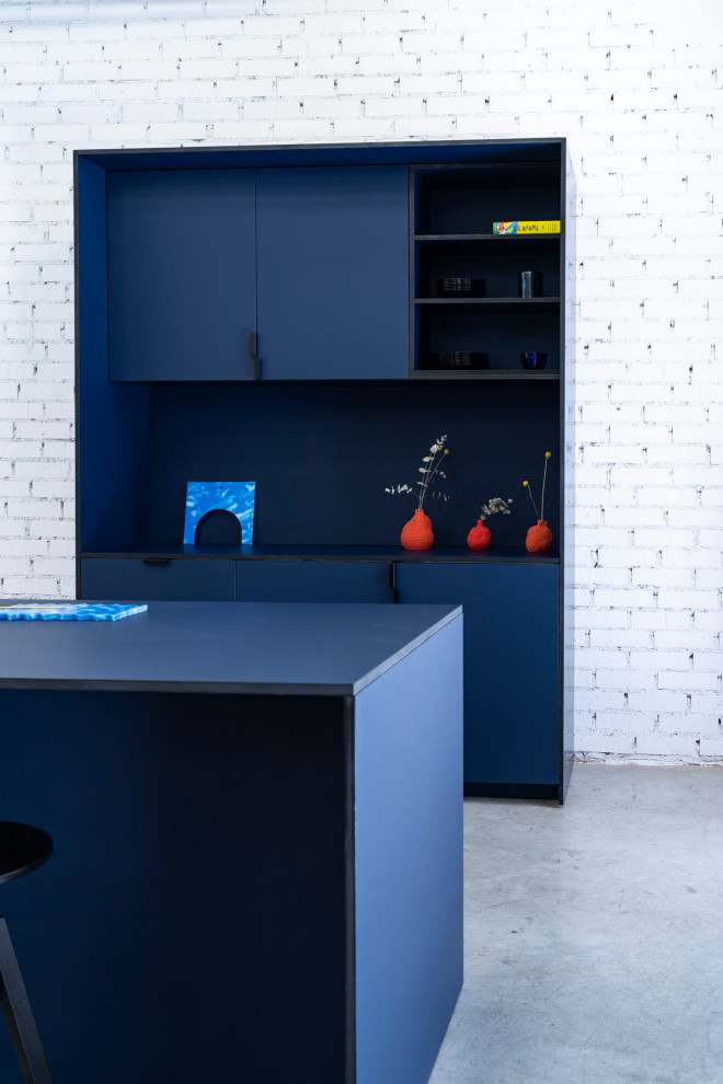 This is an example of a mid-sized industrial single-wall open plan kitchen in Madrid with a drop-in sink, beaded inset cabinets, blue cabinets, laminate benchtops, blue splashback, metal splashback, panelled appliances, concrete floors, with island, grey floor, blue benchtop and exposed beam.